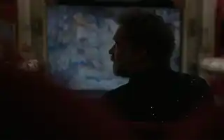 A man's profile in backlight, in the background a lit scene.