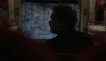 A man's profile in backlight, in the background a lit scene.