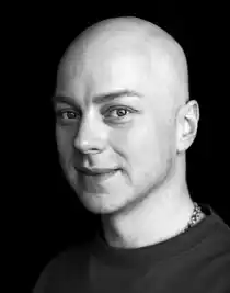 Närbild i svart-vitt på en man med mörk tröja och en halskedja.