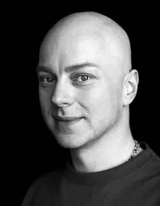 Närbild i svart-vitt på en man med mörk tröja och en halskedja.