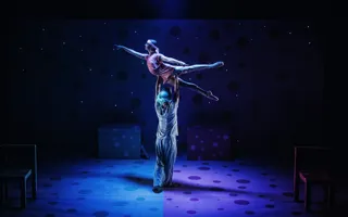 En manlig dansare lyfter en kvinnlig dansare på en mörk scen.