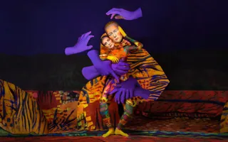 En kvinna i en färgglad kostym och med stora lila händer svävandes runt henne.