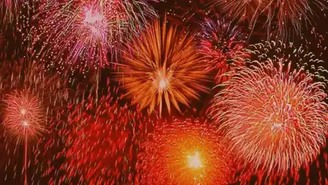 An evening sky with many fireworks in yellow and red tones.