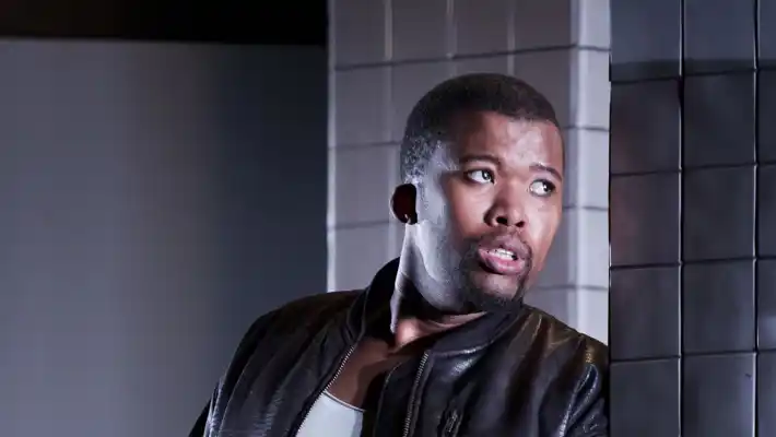 En kortklippt man i läderjacka lutar sig mot en kaklad vägg.