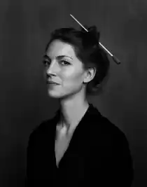 Porträttbild av en kvinna i halvprofil, hon bär en mörk kavaj och håret är uppsatt med en dirigentpinne.