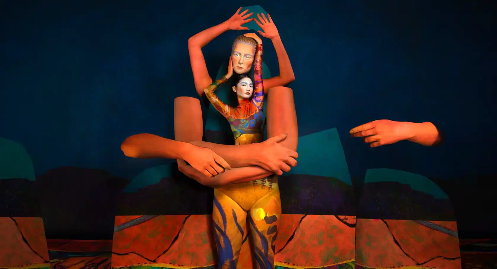 A woman holds a mask above her head, in front of her are large orange prop arms.