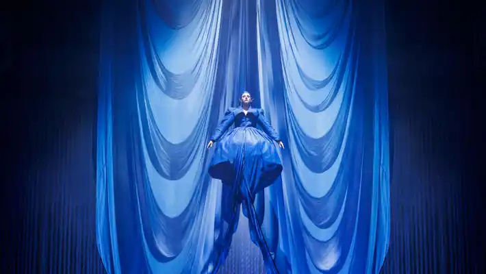 En man står på toppen av en scen under en blå ridå.