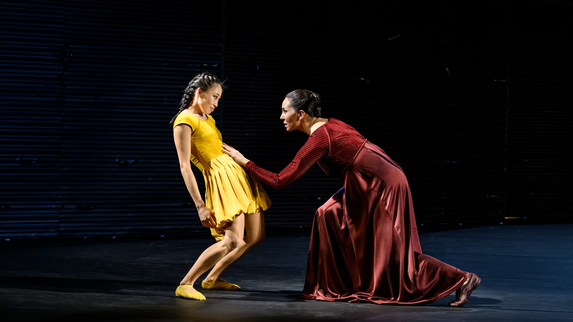 En kvinna i rött rör vid en gulklädd kvinnas mage med sin hand.