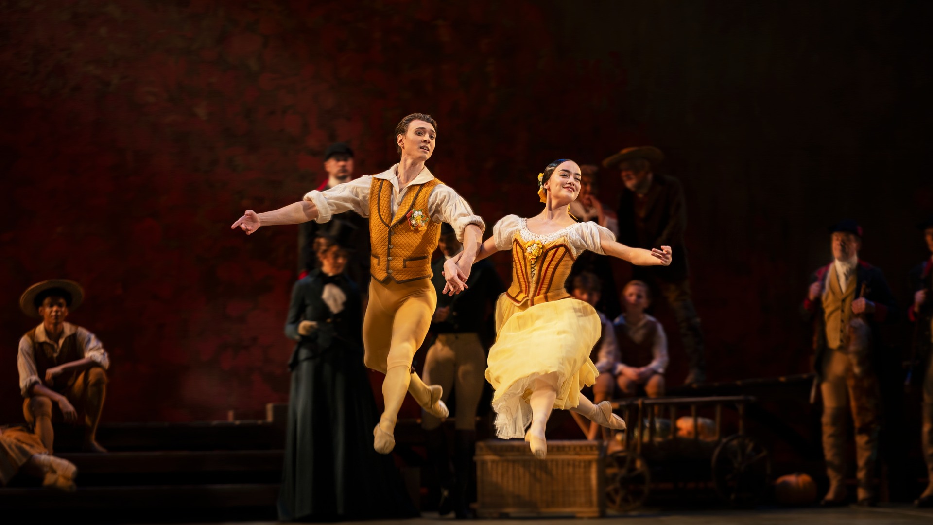 A pair of dancers, man and woman, simultaneously do a jump in the air.