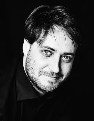 En närbild på en man med skägg mot en mörk bakgrund.