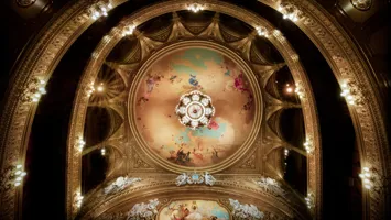 Vy över ett tak och flera balkonger, en stor takmålning och praktfull ljuskrona i mitten.