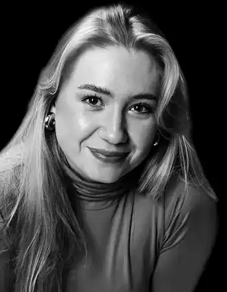 A woman with long blonde hair against a dark background.