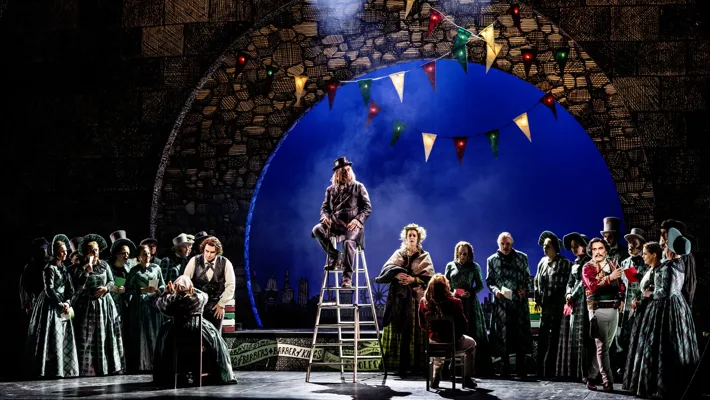 A group of people on a stage, one man sitting on a ladder.