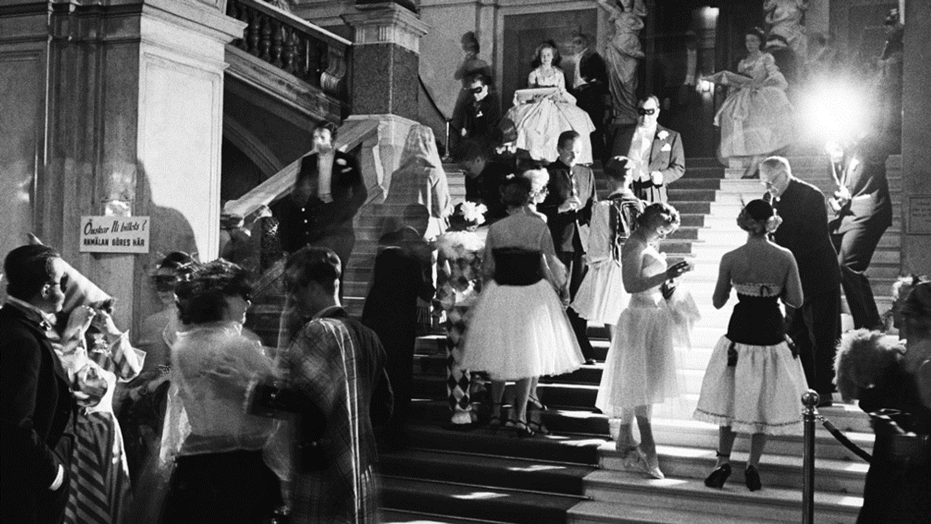 Uppför en trappa rör sig en mängd festklädda människor, en person fotar och bränner av en blixt.