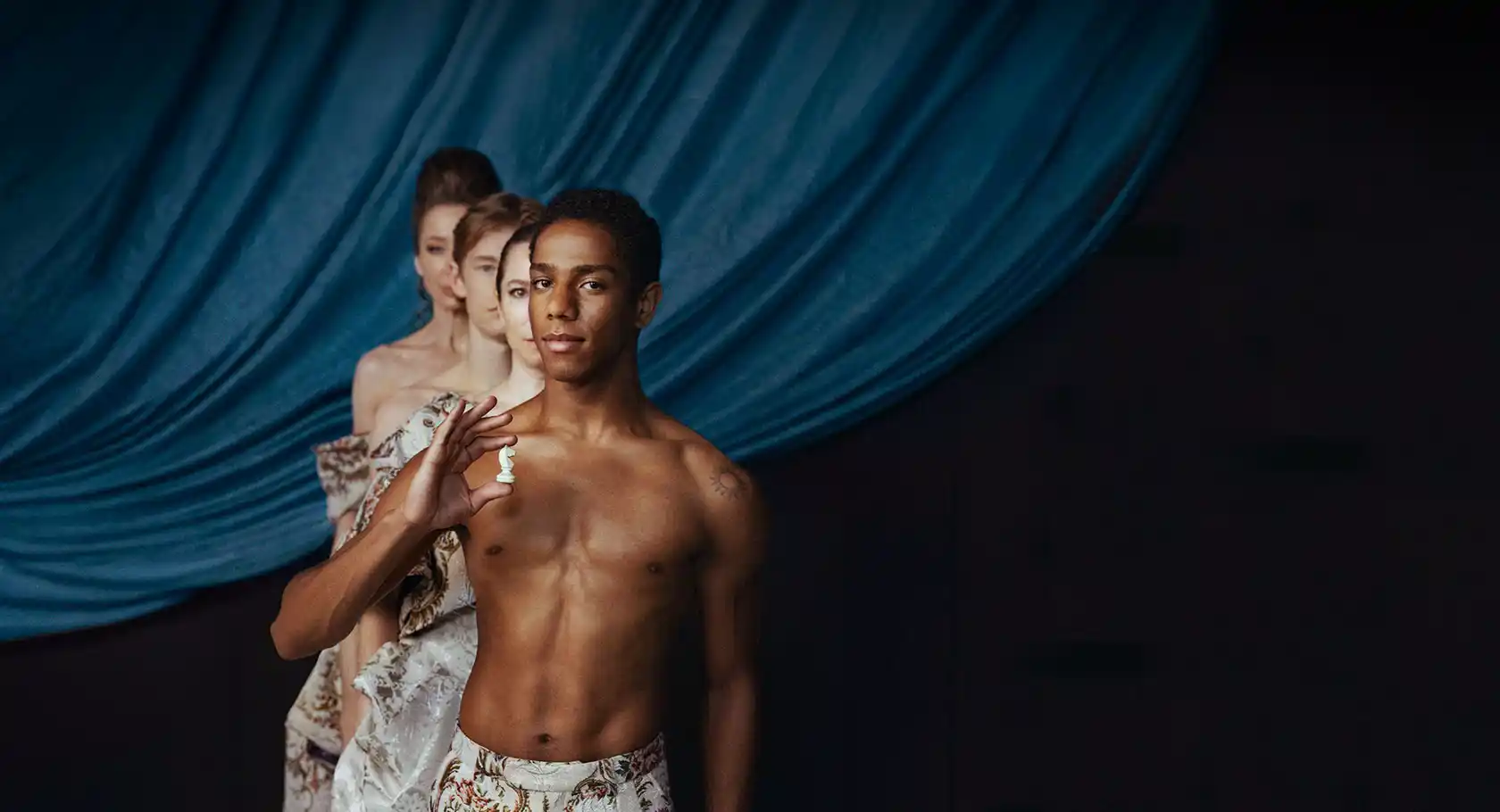 Fyra personer står i gåsarad mot ett mörkblått draperi, den första mannen håller en schackpjäs i handen.