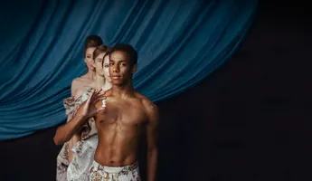 Fyra personer står i gåsarad mot ett mörkblått draperi, den första mannen håller en schackpjäs i handen.