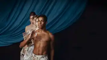 Four people stand in a row against a dark blue curtain, the first man holding a chess piece in his hand.