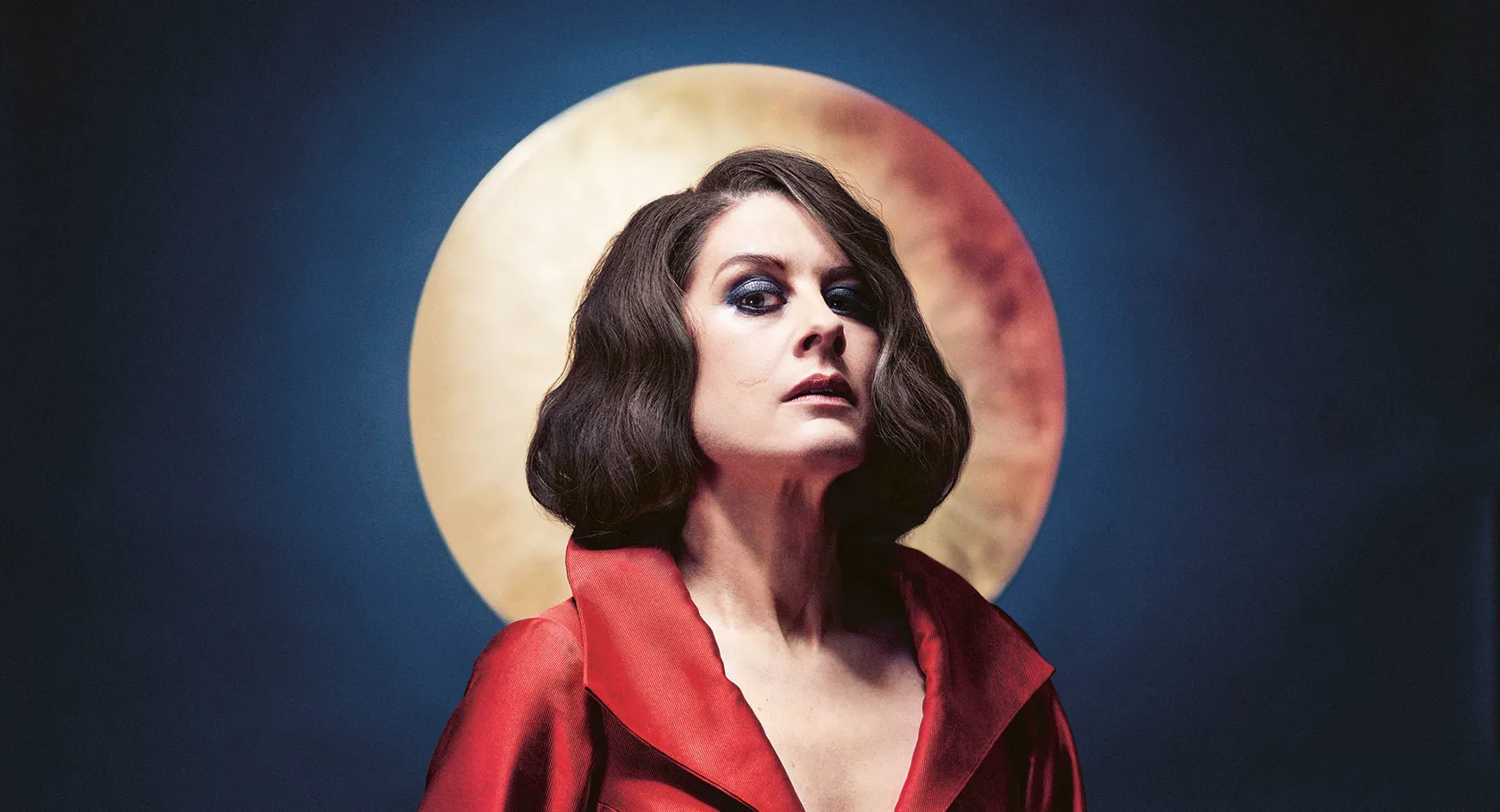 A woman in a red dress stands against a dark blue background, a moon shining behind her head.
