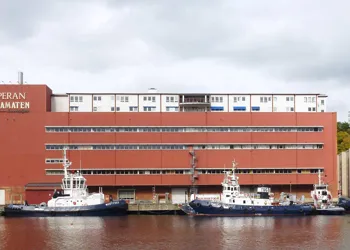 En stor rödaktig byggnad ligger vid en kaj där flera båtar ligger förtöjda.