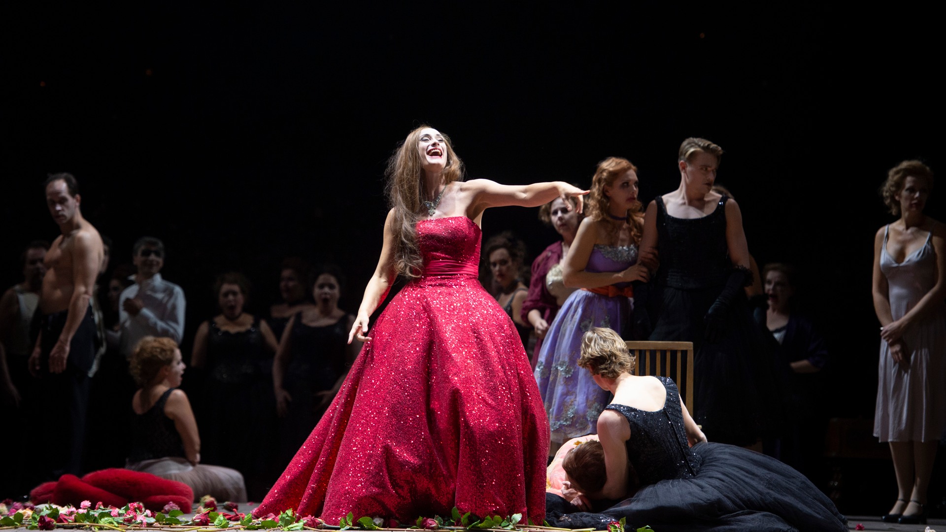 A woman in a red evening dress laughs and points her finger.