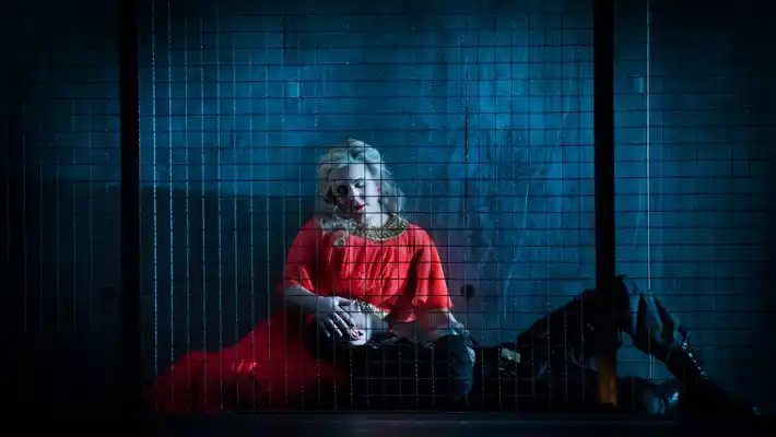 A woman dressed in red sits with a man's head in her lap behind bars.