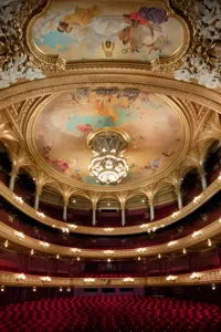 Utsikt över en stor publiksalong i flera våningar, röda stolar och många dekorationer i guld.