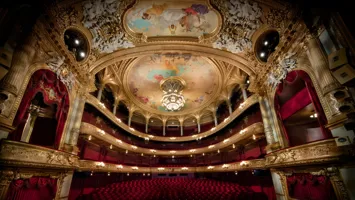 View of a large audience hall over several levels, red chairs and many gold decorations.