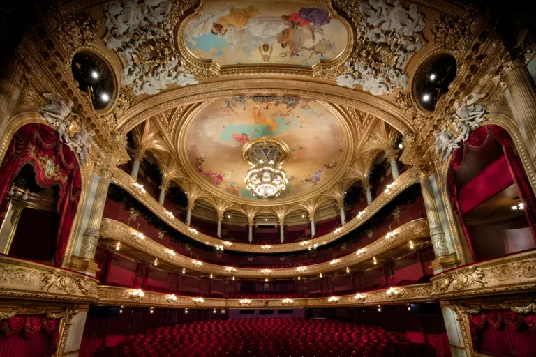 View of a large audience hall over several levels, red chairs and many gold decorations.