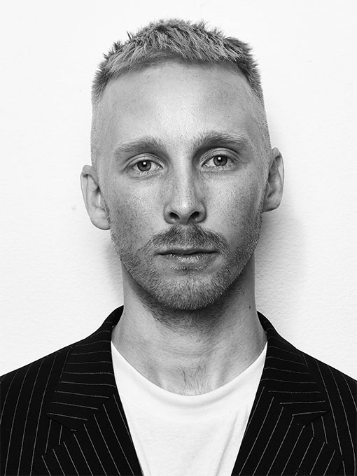 Close-up of a man with a beard and mustache wearing a striped jacket.
