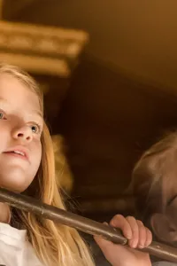 Två personer med suddade ansikten står bakom ett räcke inomhus, omgivna av varma toner.