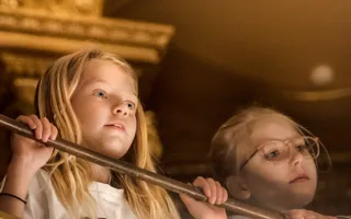 Två personer med suddade ansikten står bakom ett räcke inomhus, omgivna av varma toner.