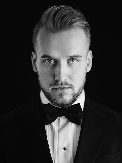 A close-up of a man wearing a suit with a white shirt and black bow tie.