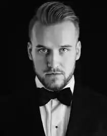 En närbild på en man som är klädd kostym med vit skjorta och svart fluga.