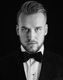 A close-up of a man wearing a suit with a white shirt and black bow tie.