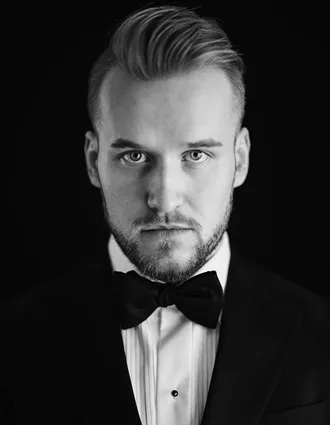 En närbild på en man som är klädd kostym med vit skjorta och svart fluga.