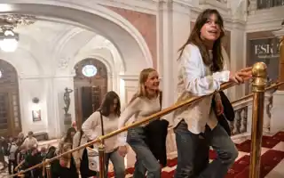 Personer går i en trappa i en elegant byggnad med valv och ljuskronor.