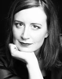 En närbild på en kvinna med långt mörkt hår, hon vilar sitt ansikte i höger hand.