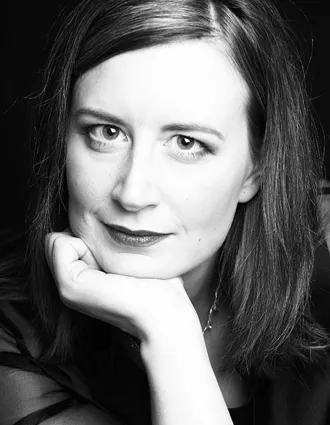 En närbild på en kvinna med långt mörkt hår, hon vilar sitt ansikte i höger hand.