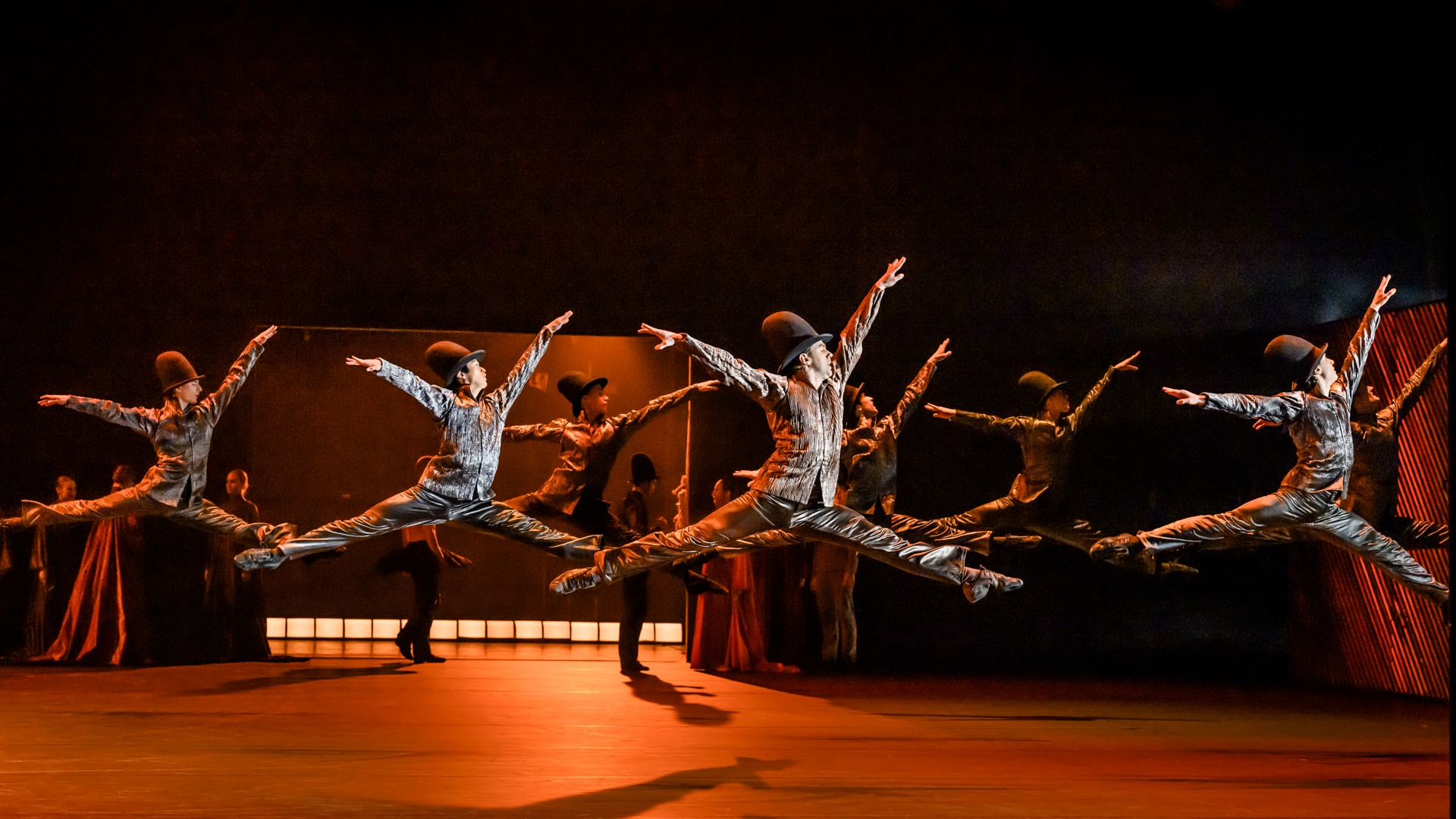 Flera manliga dansare i höga hattar hoppar samtidigt med sträckta armar och ben.