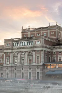 Ett stort hus vid ett vattendrag, en kyrka i bakgrunden, en lätt dimma runt byggnaderna.