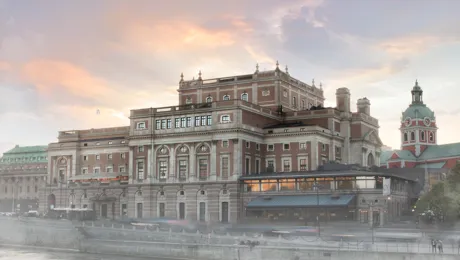 Ett stort hus vid ett vattendrag, en kyrka i bakgrunden, en lätt dimma runt byggnaderna.