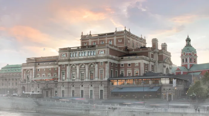 Ett stort hus vid ett vattendrag, en kyrka i bakgrunden, en lätt dimma runt byggnaderna.