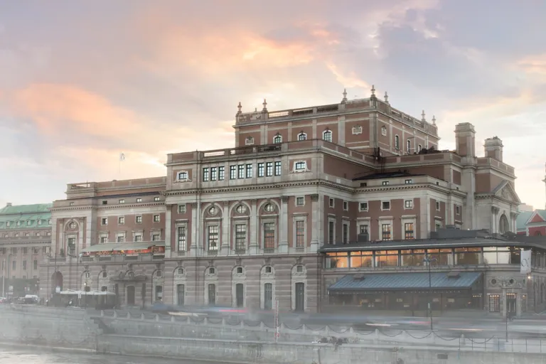 Ett stort hus vid ett vattendrag, en kyrka i bakgrunden, en lätt dimma runt byggnaderna.