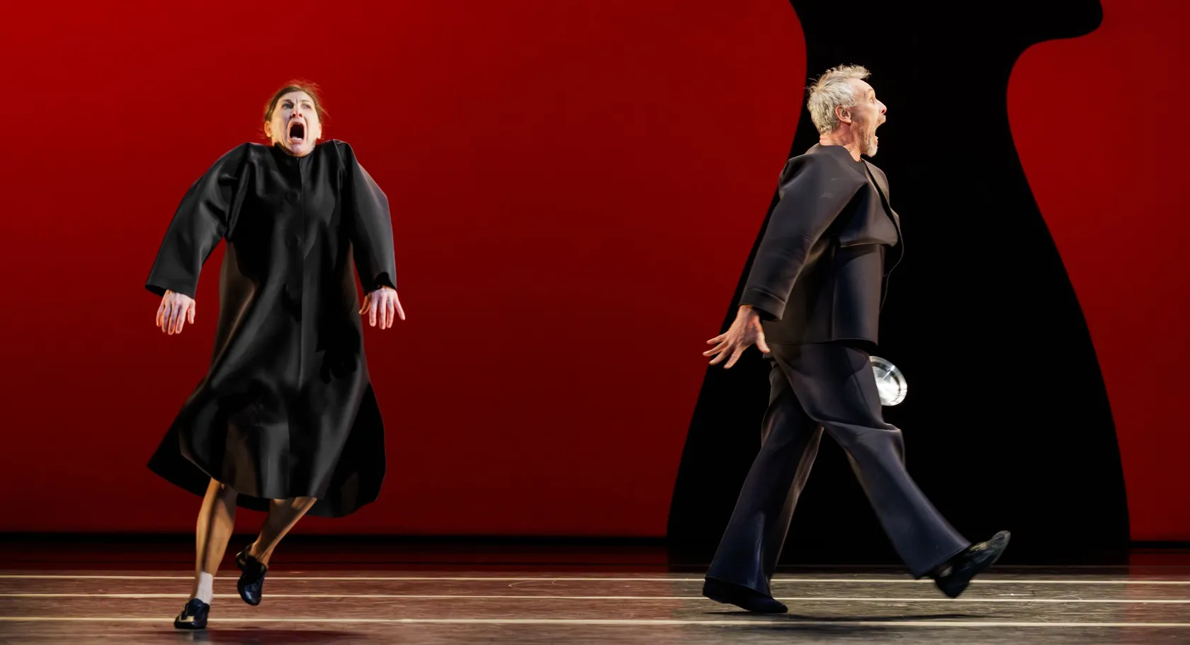 A woman and a man are moving stiffly in opposite directions against a red background.