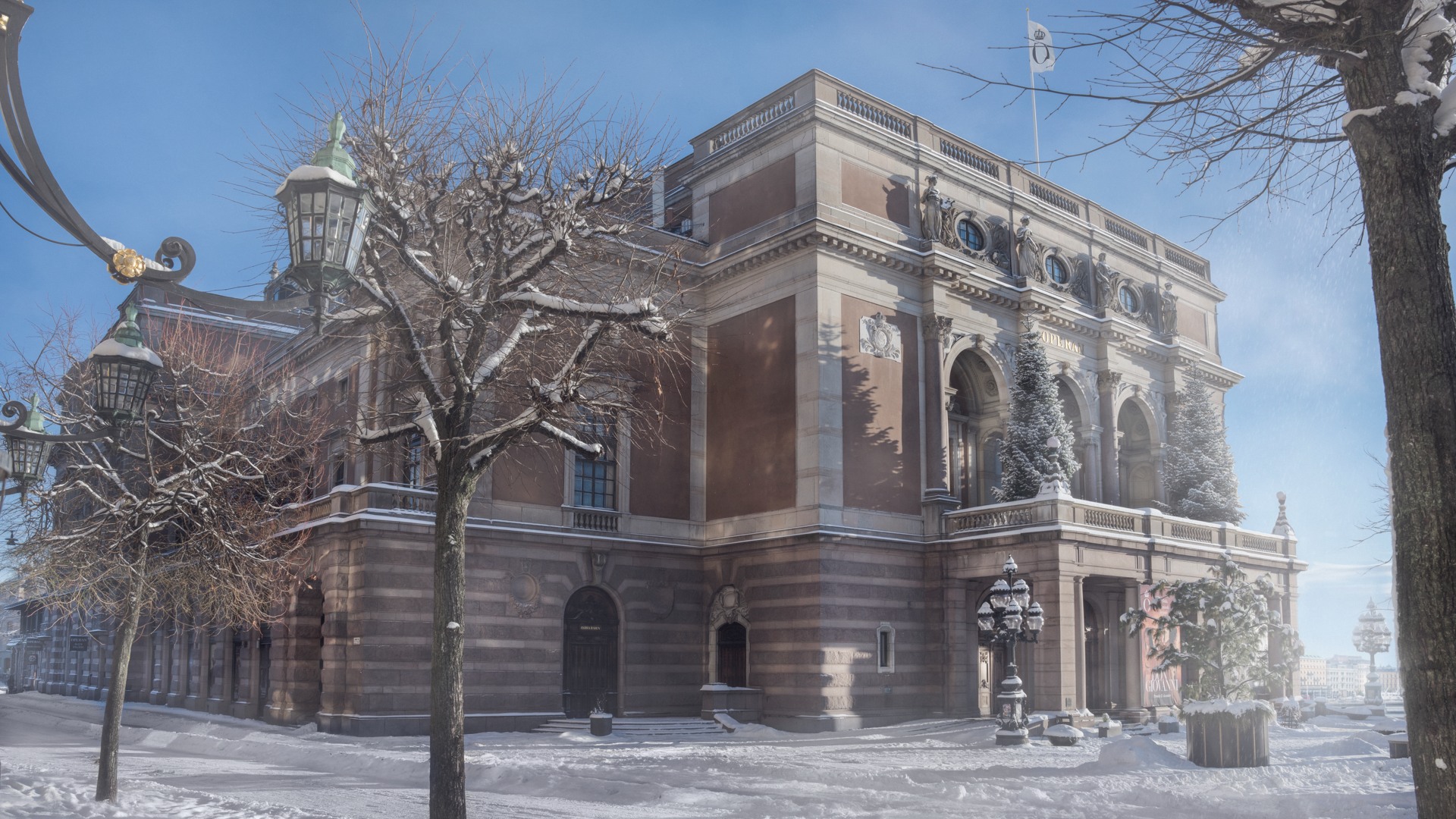 En stor byggnad mot en klarblå vinterhimmel, snö framför och på träd intill.