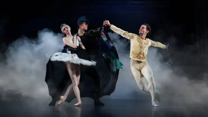 En man i mantel omfamnar en ballerina: runt dem dansar en manlig dansare.