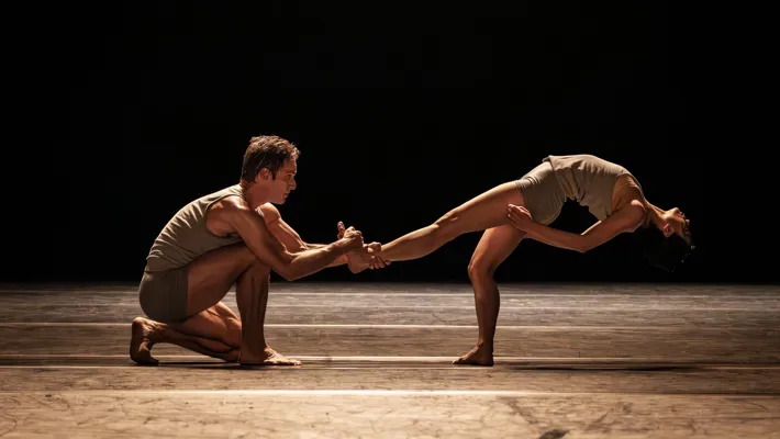 En manlig dansare på knä håller i en kvinnlig dansares fot medan hon lutar sig bakåt.