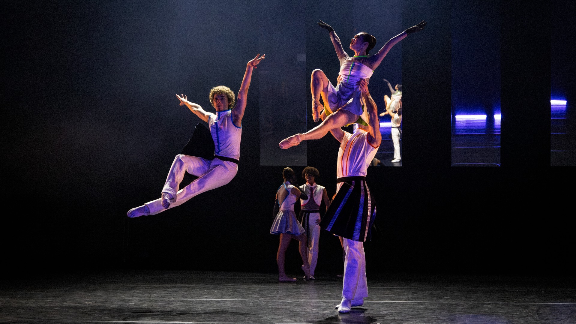 På en scen hoppar en dansare, en annan dansare lyfter en en kvinnlig dito.