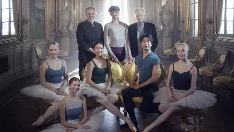 Sex unga dansare flankerade av två äldre herrar i ett ljusfyllt rum.