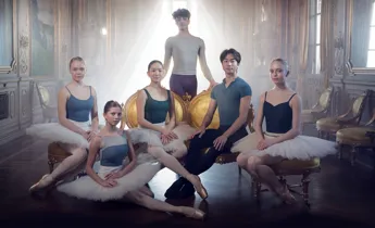 Sex stycken dansare samlade i ett bakgrundsbelyst rum.